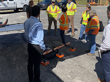 Man explaining to several people wearing personal protection equipment outdoors how to use a dielectric profiling system.